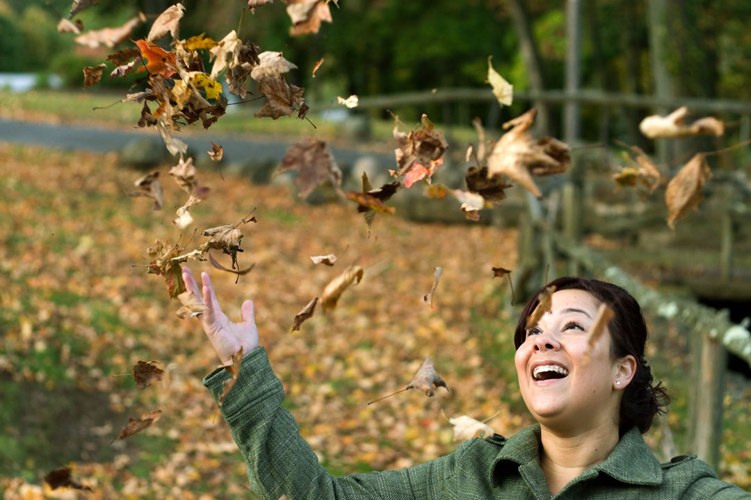 Woman Laughing As The Leaves Fall All Around Her During The Autumn Season